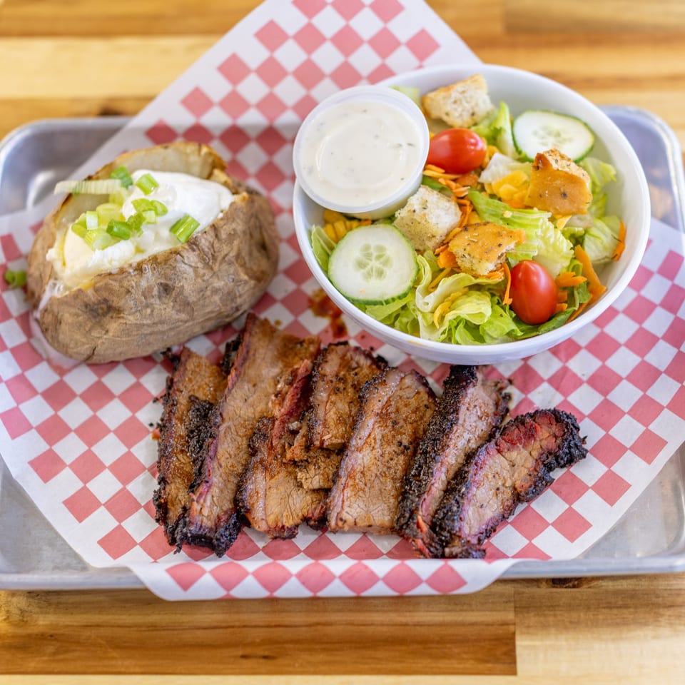 Dave's BBQ & Smokehouse brisket plate with a baked potato and side salad on a metal tray.