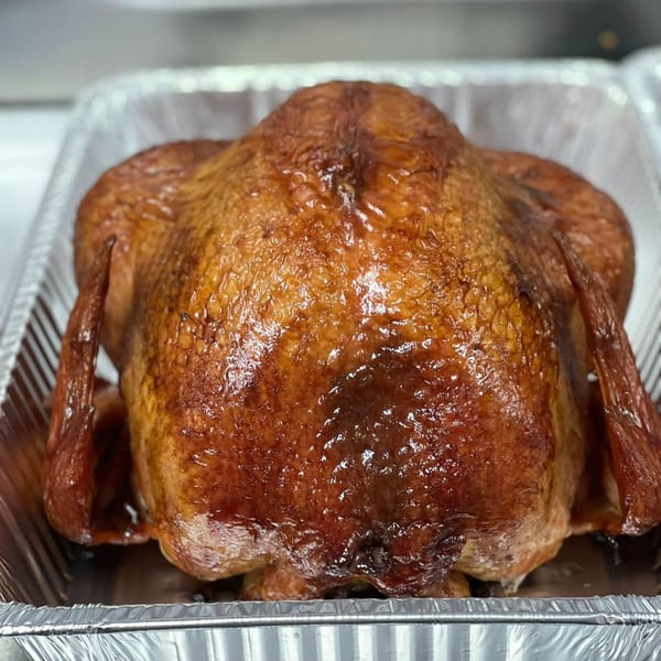 Whole roasted turkey with crispy, golden-brown skin in a foil pan from Dave's BBQ & Smokehouse.