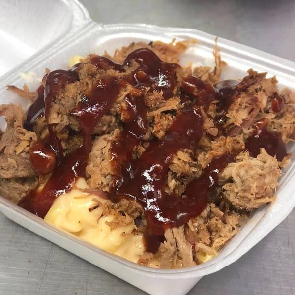 Dave's BBQ & Smokehouse pulled pork and mac and cheese, drizzled with barbecue sauce in a takeout container.