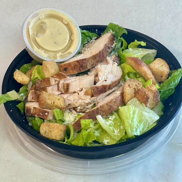 Dave's BBQ & Smokehouse Caesar salad with sliced chicken, croutons, and dressing in a black bowl.