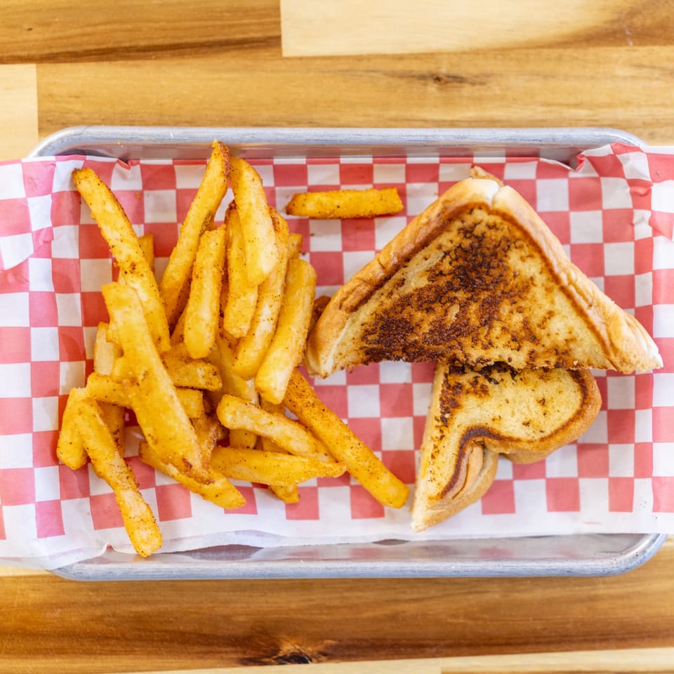 Dave's BBQ & Smokehouse grilled cheese sandwich and seasoned fries on a checkered paper-lined tray.